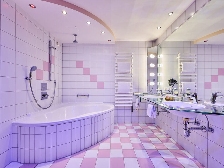 Helles Hotelbad mit Eckbadewanne, beleuchtetem Spiegel, Glas-Doppelwaschtisch und Handtuchwärmer.