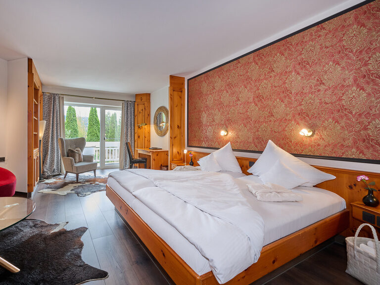 Geräumiges Hotelzimmer mit Doppelbett, Sofa und Balkonblick ins Grüne.