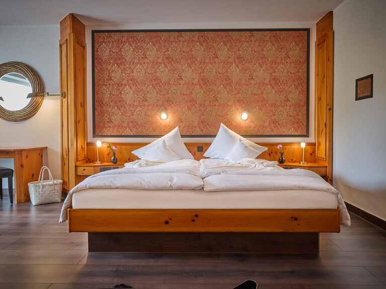 Hotelzimmer mit Doppelbett, eleganter Wandtapete, Holzinterieur und dekorativem Wandbild in orange.
