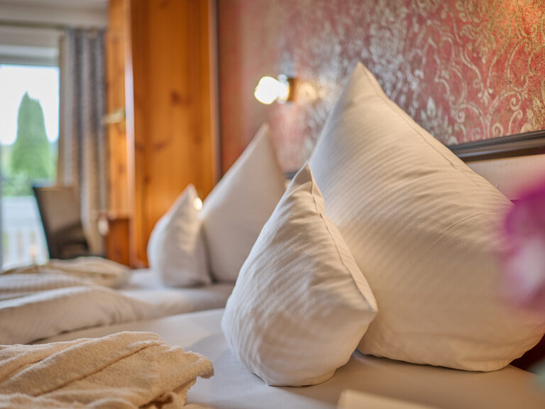 Reihe weiß gestreifter Kopfkissen vor rotgoldener Tapete mit Balkonlicht im Hintergrund.