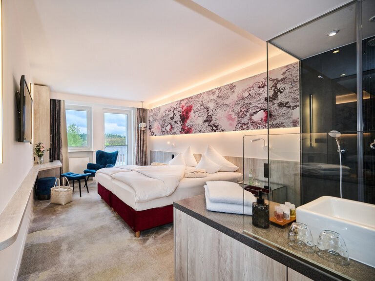 Modernes Hotelzimmer mit Doppelbett, offenem Bad und blauen Sesseln.