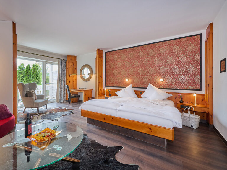 Geräumiges Hotelzimmer mit Sitzecke, Doppelbett, Holzelementen und Balkonblick.