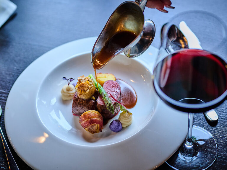 Feines Fleischgericht mit Sauce, Gemüse und Rotwein auf elegant gedecktem Tisch im Restaurant.