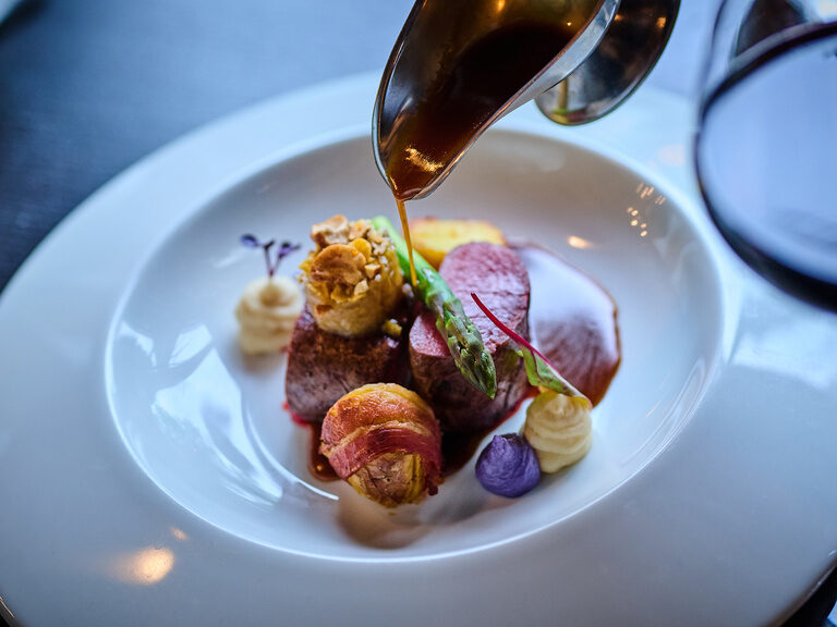 Zartes Filet mit Gemüse, Kartoffeln und Sauce auf weißem Teller angerichtet.