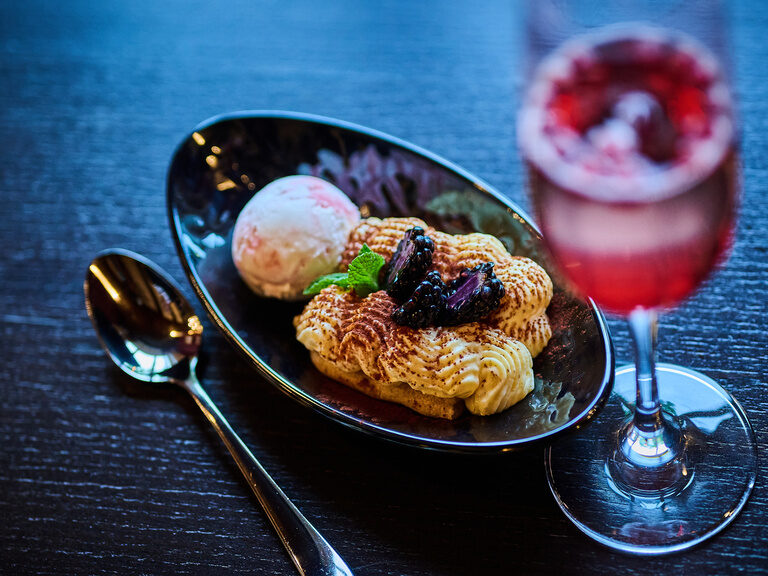 Dessert mit Eis, Brombeeren und Getränk auf dunklem Holztisch.