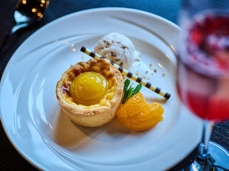 Dessert mit Eistörtchen, Kugel Vanilleeis, Minze und Mandarinenfilets auf weißem Teller.