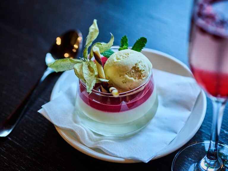 Dessert mit Eis, roter Geleeschicht und Physalis in Glas serviert auf Unterteller.