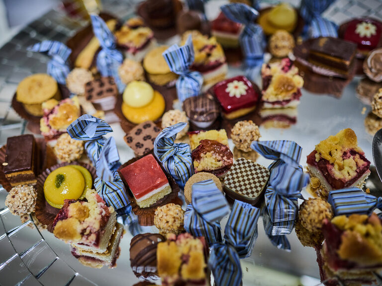 Bunt gemischte Petit Fours und Pralinen auf silbernem Tablett mit Dekoband arrangiert.