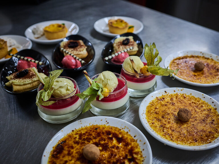 Auswahl edler Desserts mit Eis und Crème brûlée auf Edelstahltisch angerichtet.