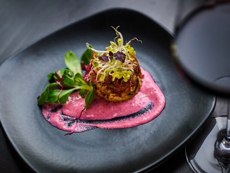 Gourmet-Vorspeise auf rosa Creme mit Kräutern und Microgreens auf schwarzem Teller..