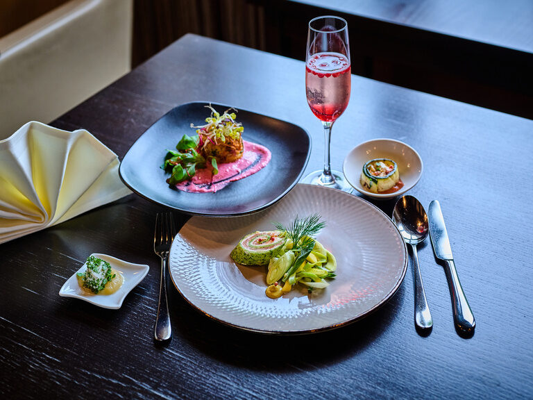 Vorspeisenteller mit Lachsroulade, Gemüse und rosarotem Drink auf edlem Tisch.