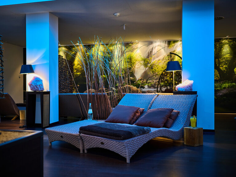 Ruhiger Wellness-Raum mit Liege, indirekter Beleuchtung und Naturmotiv.