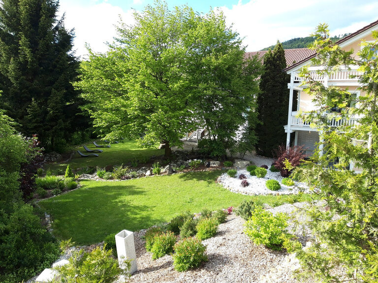 Sonniger Hotelgarten mit Liegewiese, Ziersträuchern und Balkonen im Hintergrund.