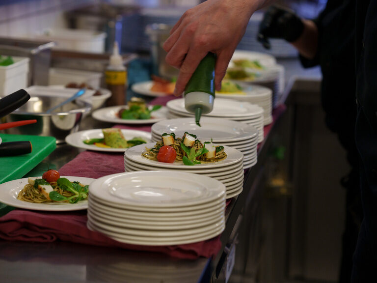 Hand verziert Pastateller mit grünem Dressing in Restaurantküche.