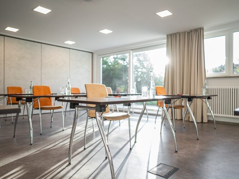 Tageslichtdurchfluteter Konferenzraum mit Stühlen, Wasserflaschen und Block.