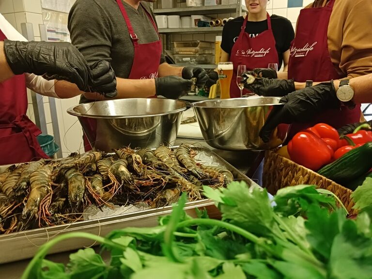 Mitarbeiter der Küche bereiten Garnelen in Kochkurs mit Schürzen, Handschuhen und frischem Gemüse zu.