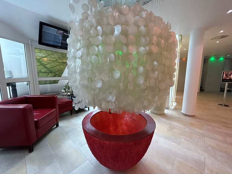 Organisch geformte Lichtinstallation aus weißen Plättchen über rotem Sockel in heller Lounge.