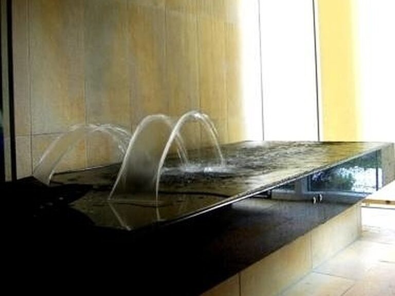 Leere Steinliege mit drei gebogenen Wasserstrahlen unter breitem Duschkopf.