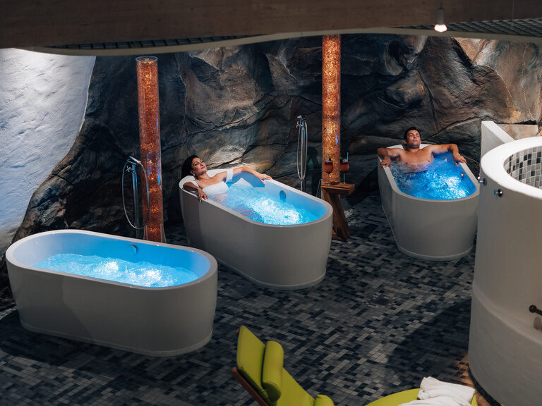 Zwei Personen entspannen in Whirlwannen vor Felskulisse in Spa-Landschaft.