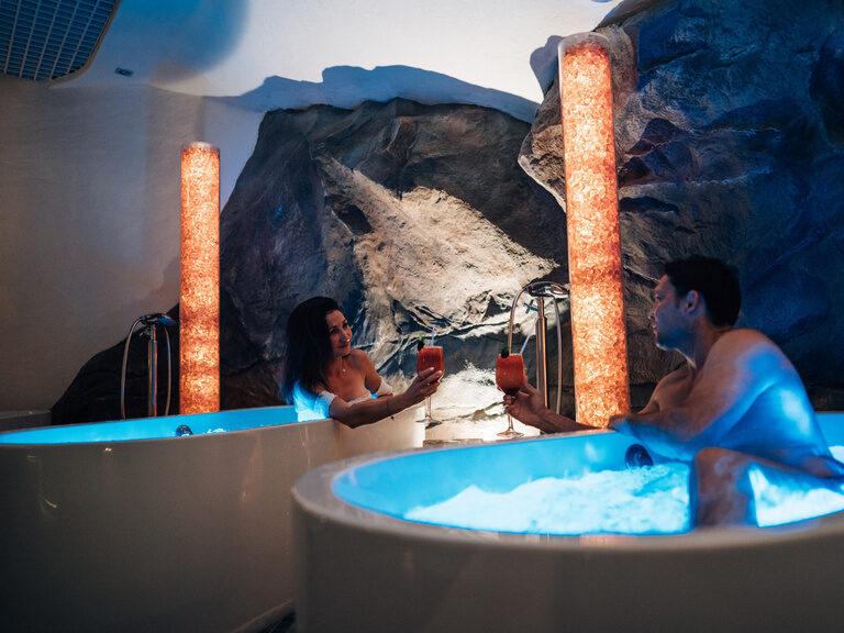Paar entspannt mit Cocktails in separaten Whirlwannen, gemütliche Wellness-Atmosphäre.