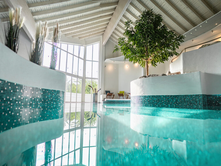 Heller Innenpool mit Tageslicht, moderner Architektur und grünen Pflanzen im Wellnessbereich.