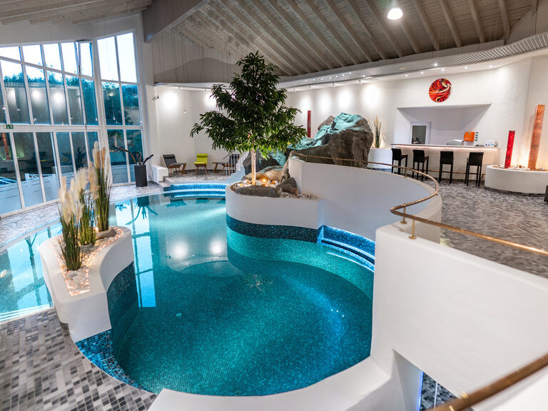 Innenpool mit Bar, Pflanzeninsel und Panoramafenstern in modernem Ambiente.