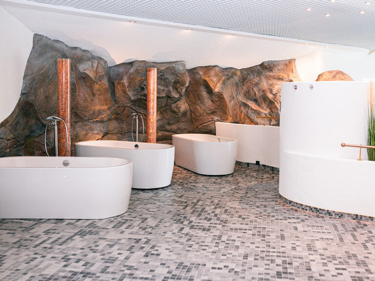 Mehrere freistehende Badewannen vor Felswand, sanft beleuchtet und modern gestaltet.