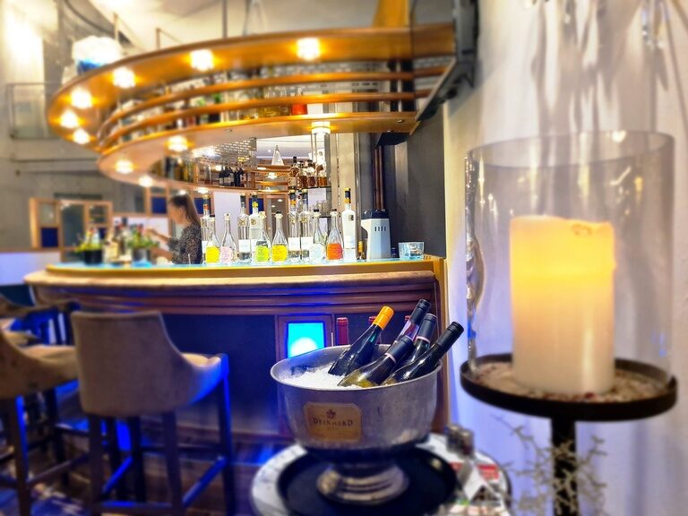 Hotelbar mit Flaschen auf Eis, Kerzenlicht und bunt etikettierten Spirituosen im Regal.