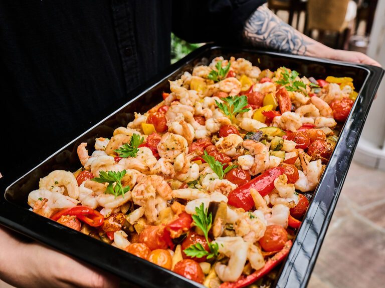 Großes Tablett mit Garnelen und geröstetem Gemüse wird getragen.