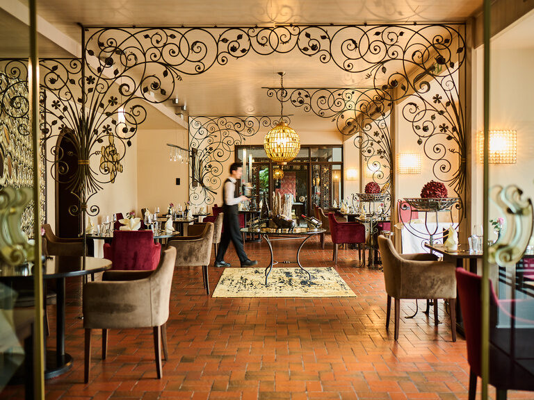 Stilvoller Restaurantraum mit verziertem Schmiedeeisen und Servicepersonal in Bewegung.