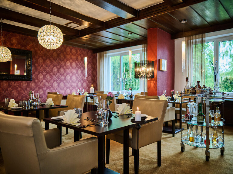 Elegantes Hotelrestaurant mit gedeckten Tischen, Lederstühlen und Blick auf grüne Gartenanlage.