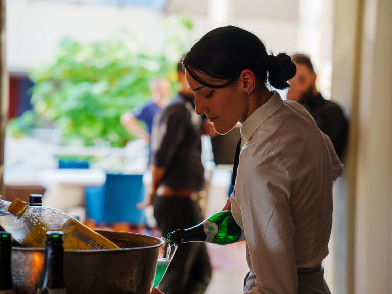 Servicekraft in weißem Hemd schenkt grünes Getränk bei Veranstaltung ein.