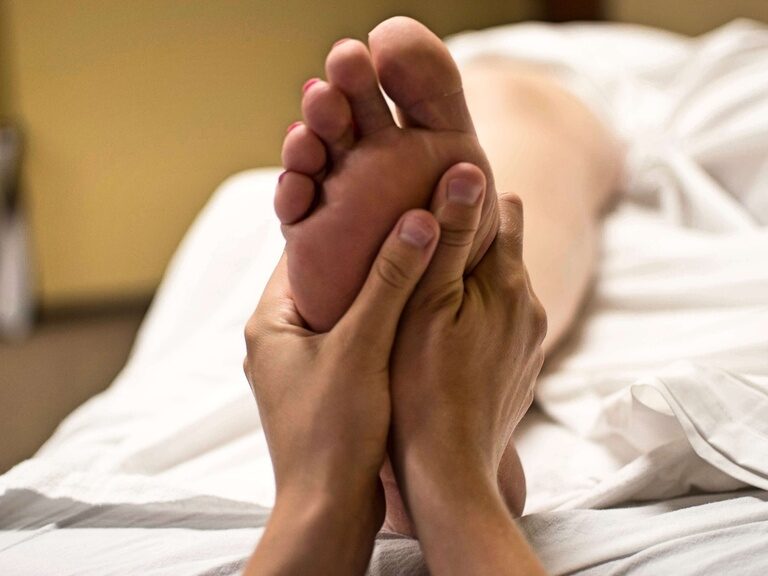 Zwei Hände massieren sanft die Fußsohle einer liegenden Person.