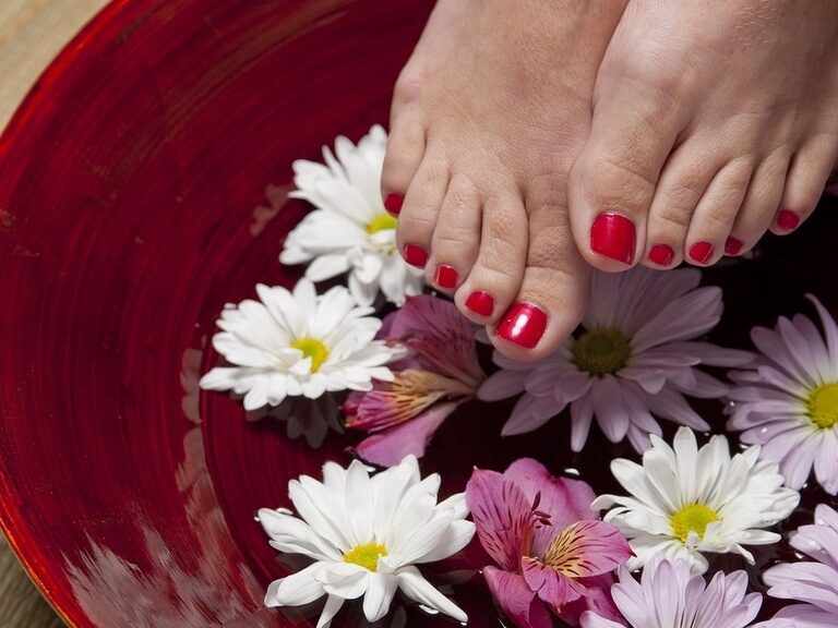 Füße mit rotem Nagellack in Schale mit Wasser und Blüten.