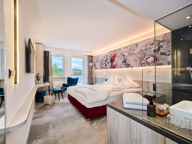 Elegantes Hotelzimmer mit integriertem Bad, moderner Ausstattung und blauen Sesseln.