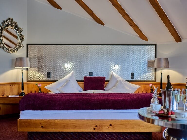 Frontale Bettansicht mit purpurroter Tagesdecke, Wandlampen und Spiegel links.