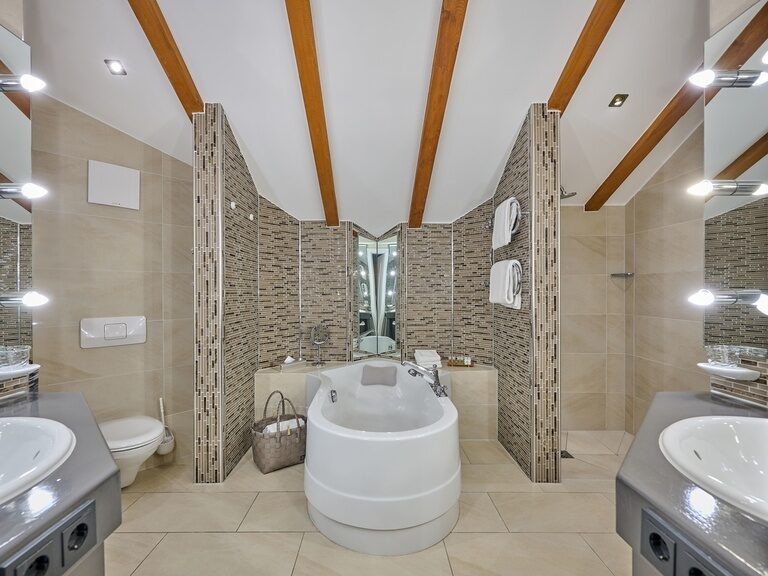 Modernes Bad mit freistehender Badewanne, Spiegelwand und Dachschräge mit Holzbalken.