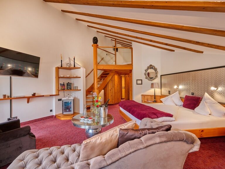 Zimmer mit Doppelbett, Couch, TV, Treppe zu Schlafbereich auf Empore.