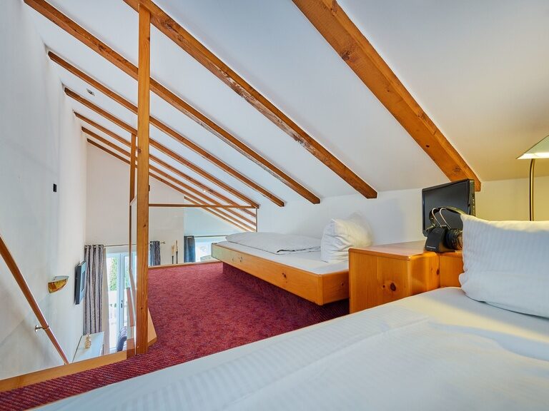Empore mit zwei Einzelbetten unter Dachschräge mit Holzbalken.