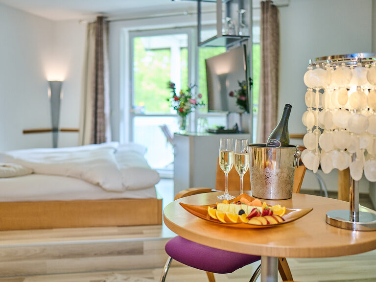 Runder Holztisch mit Obstplatte, Sektgläsern, Champagnerkühler und Muschel-Lampe vor Bett.