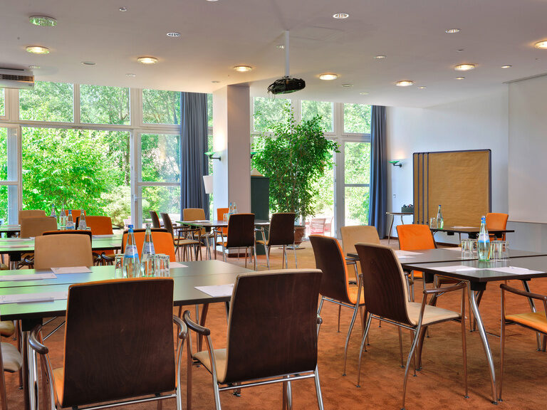 Moderner Seminarraum mit großen Fenstern, Einzelplätzen und Flipchart.