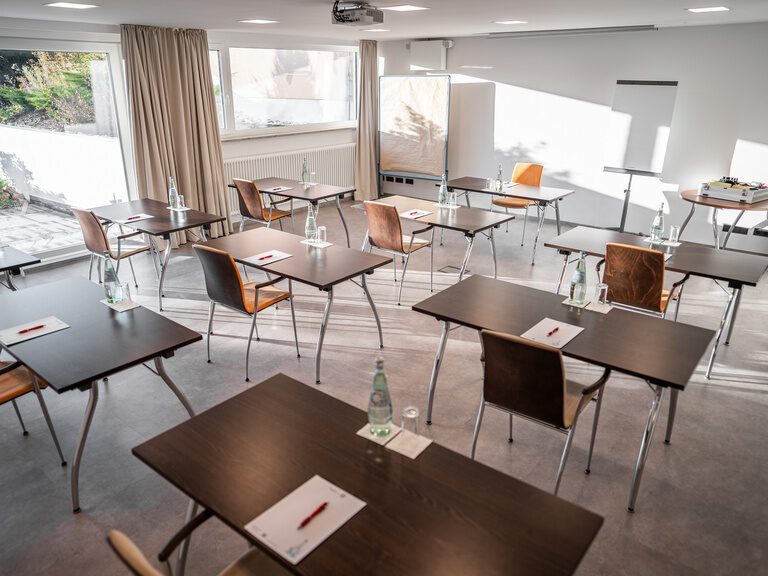 Heller Tagungsraum mit Stuhlgruppen, Glasflaschen und Ausblick ins Grüne.