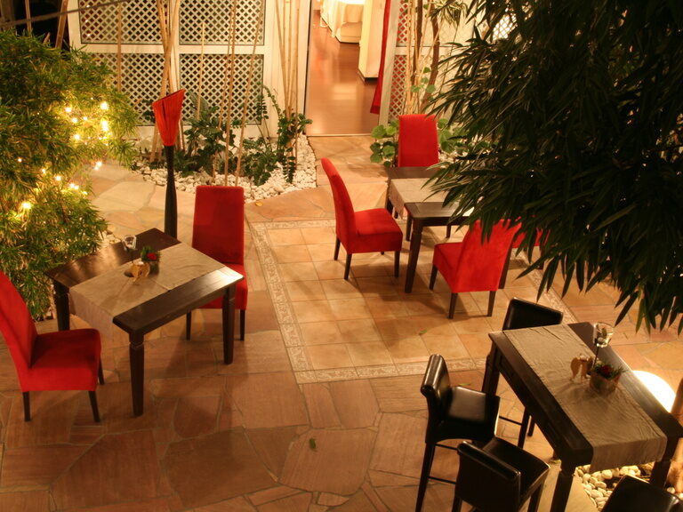 Innenhof mit dunklen Tischen, roten Stühlen und stimmungsvoller Beleuchtung.