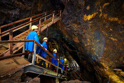 Besucher in Schutzkleidung auf Holzstegen in beleuchteter Tropfsteinhöhle.