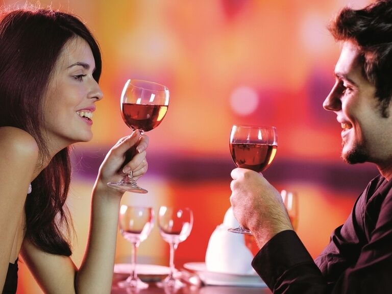 Romantischer Moment, bei dem ein Mann und eine Frau lächelnd mit Weingläsern anstoßen.