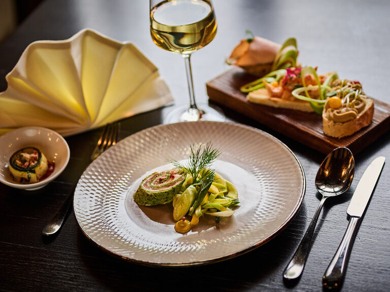 Elegante Vorspeise auf weißem Teller angerichtet mit Weißwein und Besteck.