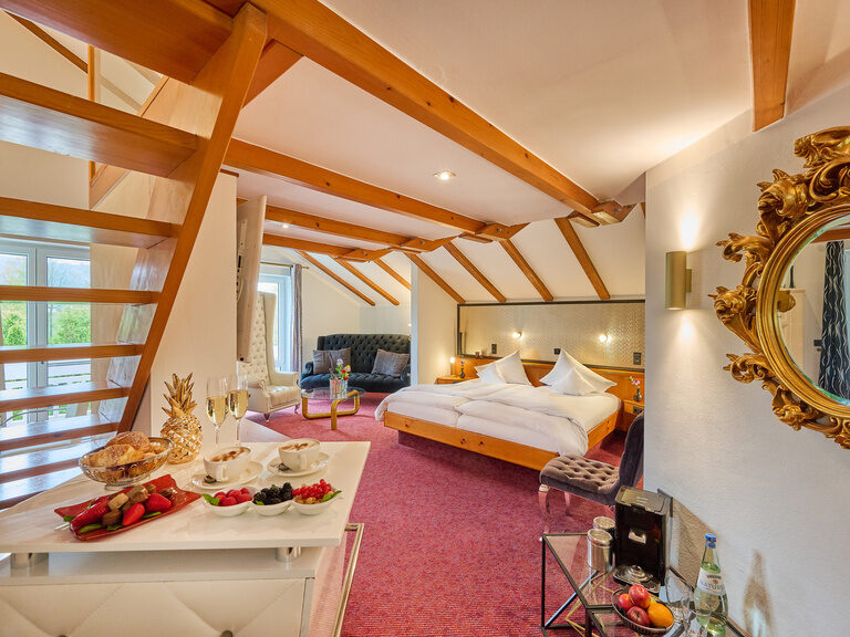 Zimmer mit offener Holztreppe, Doppelbett und Obstarrangement auf Anrichte.