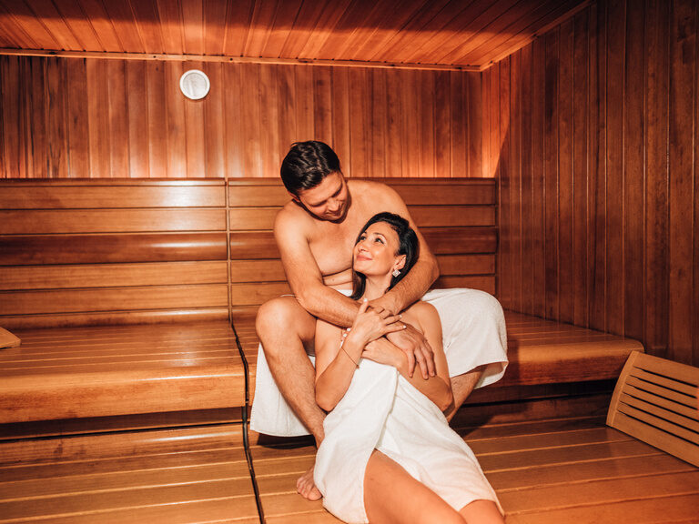 Paar entspannt in holzverkleideter Sauna mit indirekter Beleuchtung.