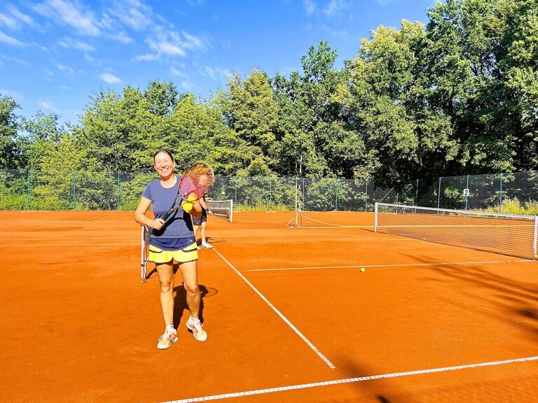 Glückliche Tennisspielerin steht lächelnd auf einem Sandplatz.