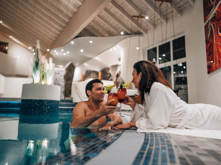 Paar entspannt am Poolrand mit Getränken in einer stilvollen Badelandschaft.
